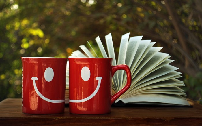 Two red mugs with smiley faces and an open book