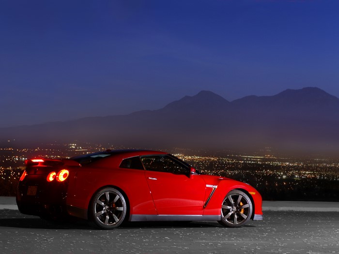Red Nissan GT-R at night with city lights and mountains
