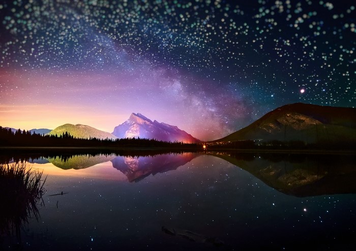Starry night sky over mountains and lake reflection