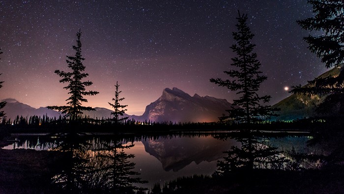 Starry night over a lake with mountains and trees