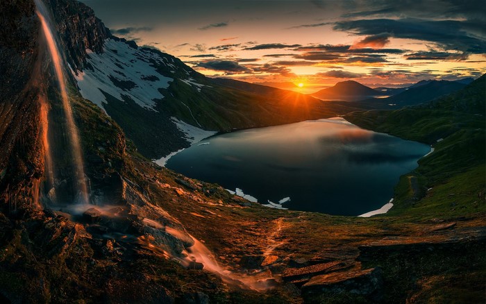 Sunset over a mountain lake with a waterfall