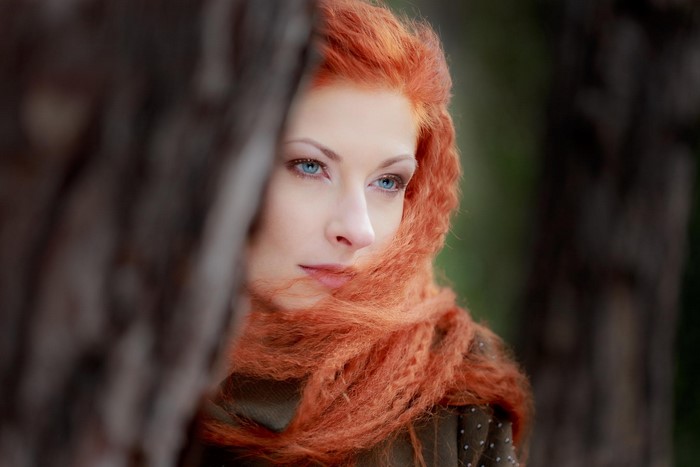 Woman with red hair and blue eyes behind a tree