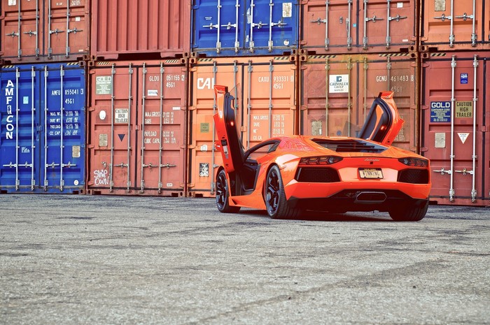Orange Lamborghini Aventador parked near shipping containers