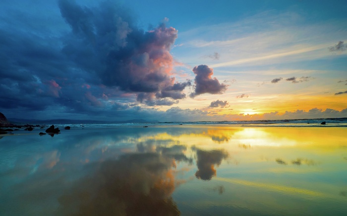 Sunset over a reflective beach with dramatic clouds