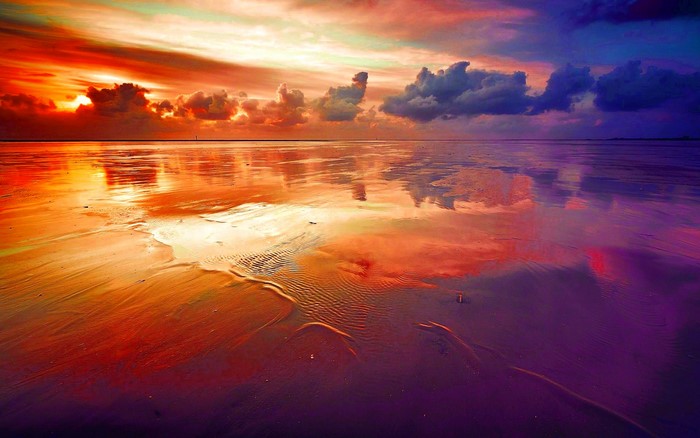 Sunset over a wet sandy beach with colorful clouds