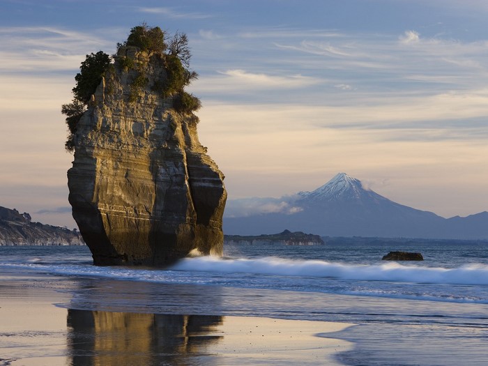 Rock formation on a beach with a volcano in the background