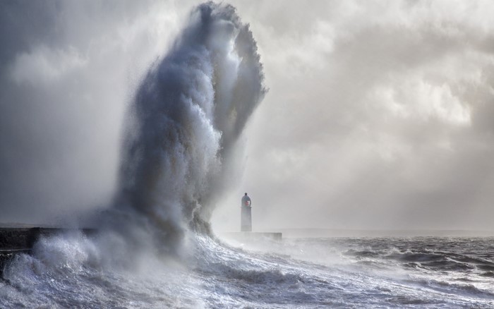 Massive wave crashing near a lighthouse during a storm
