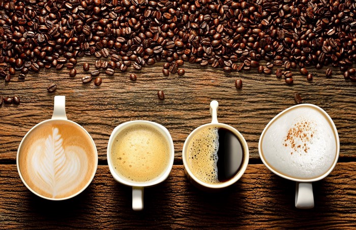 Four cups of coffee and coffee beans on a wooden table