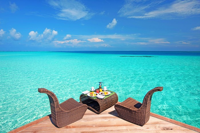 Breakfast table for two on a wooden deck overlooking turquoise ocean