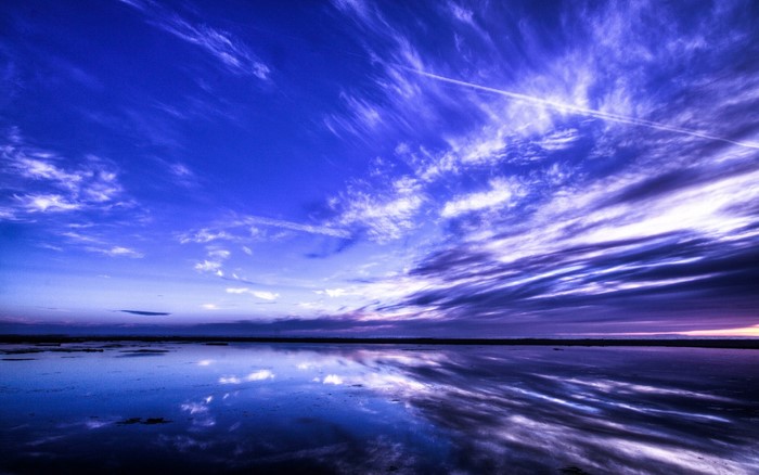 Vast blue sky with wispy clouds reflected in calm water