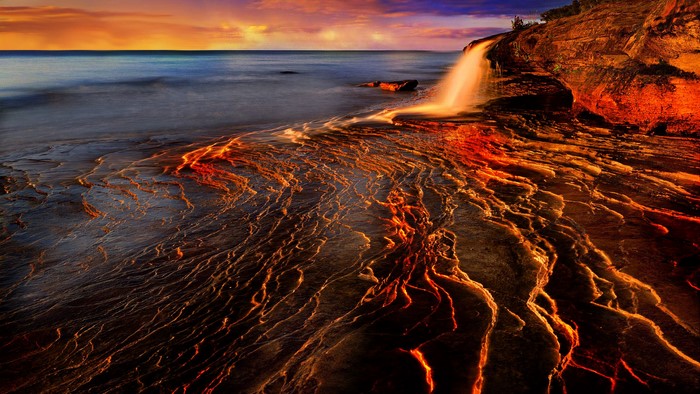 Waterfall over rocky shore at sunset
