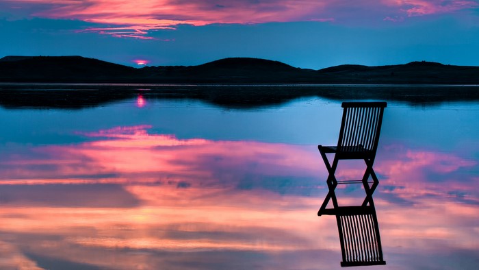 Chair reflected in water at sunset