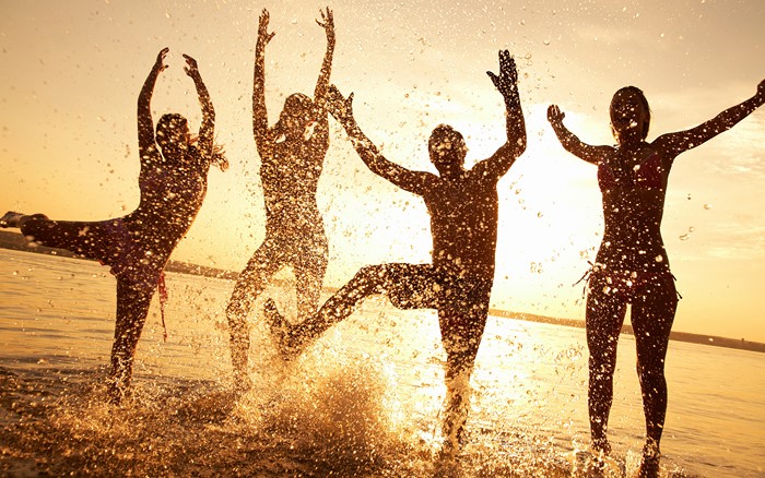 Four people jumping in water at sunset