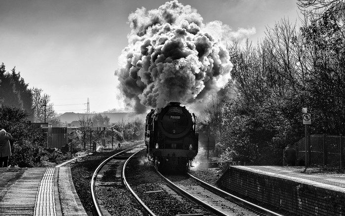 Steam train emitting large cloud of smoke on railroad tracks