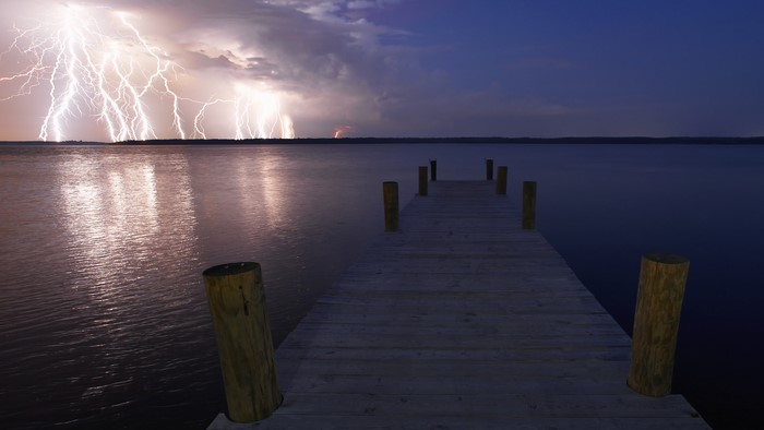 Lightning strikes over a lake with a wooden pier