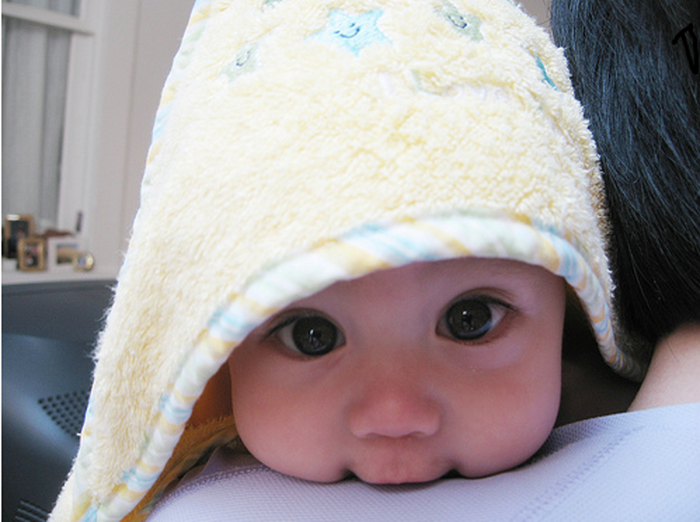 Baby peeking from under a yellow hooded towel