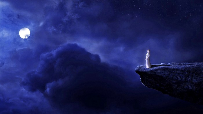 Woman on cliff edge under moonlit sky