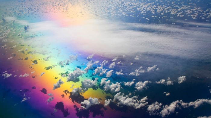 Aerial view of rainbow reflection on ocean with clouds