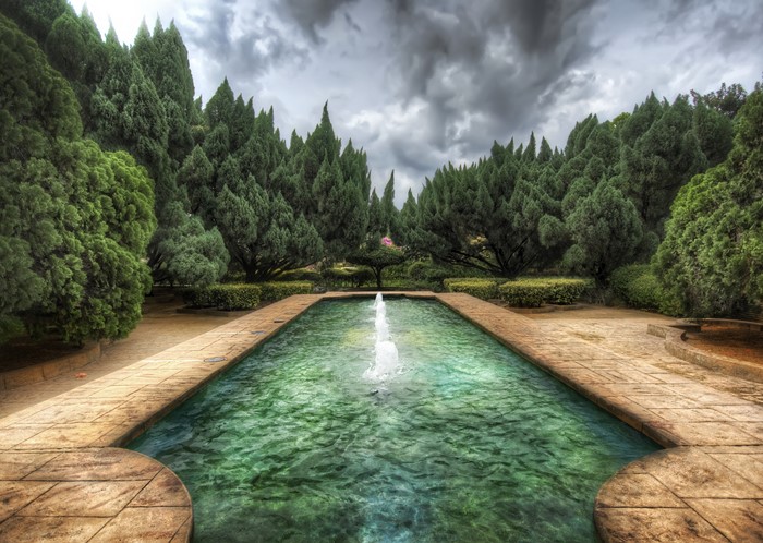 Rectangular pool with fountain in a garden with cypress trees