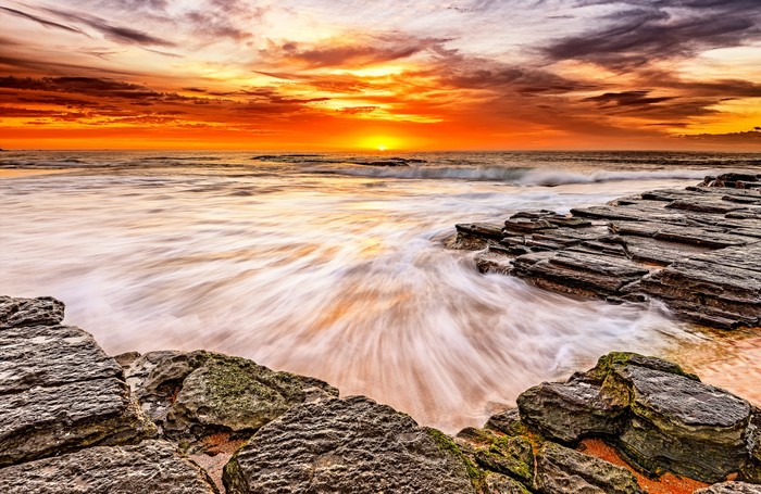 Sunset over the ocean with rocks and waves