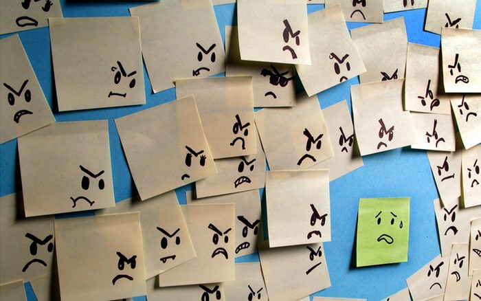 Many angry faces on sticky notes, one sad face