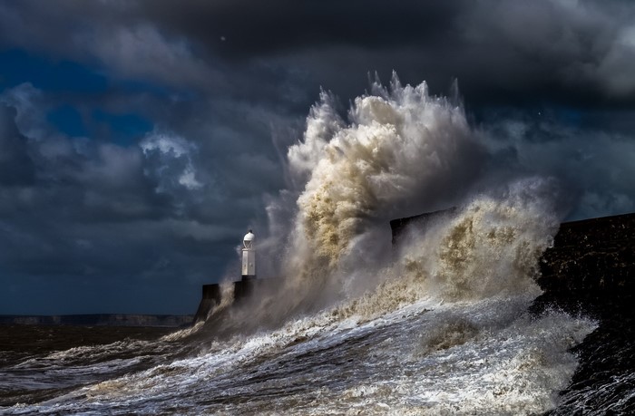 Stormy ocean waves crashing against a lighthouse and pier