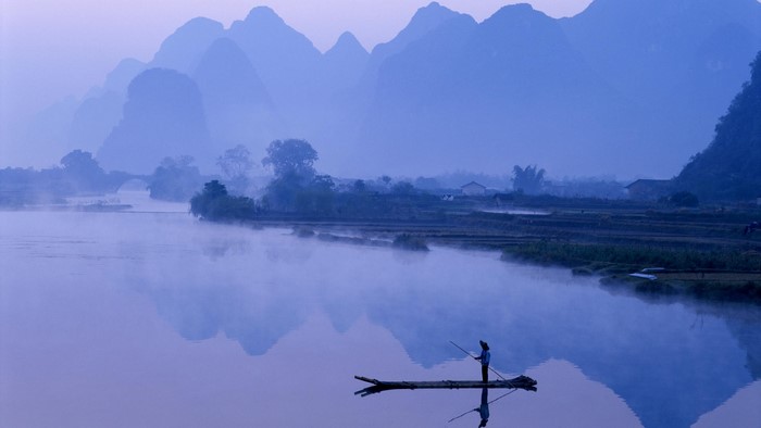 Fisherman on a raft on a misty river with karst mountains