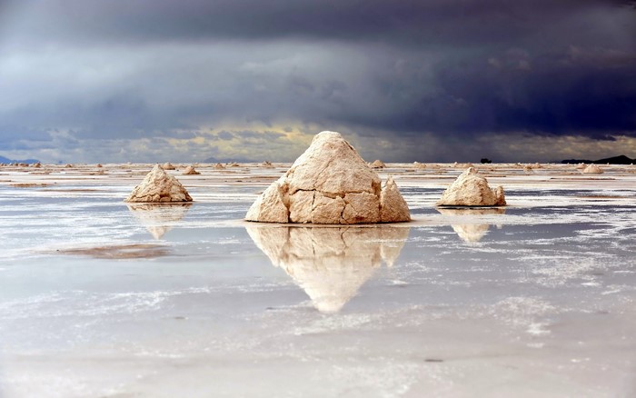 Salt piles in a reflective salt flat under stormy clouds