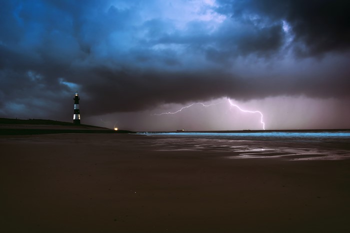 Lightning strikes over the ocean near a lighthouse at night