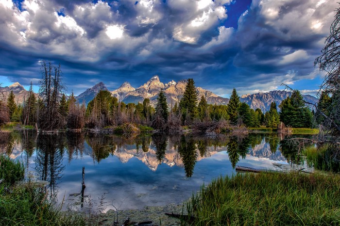 Lake reflection of mountains and trees under cloudy sky