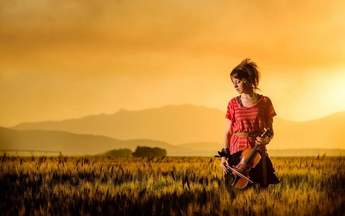 Lindsey Stirling with violin in a field at sunset