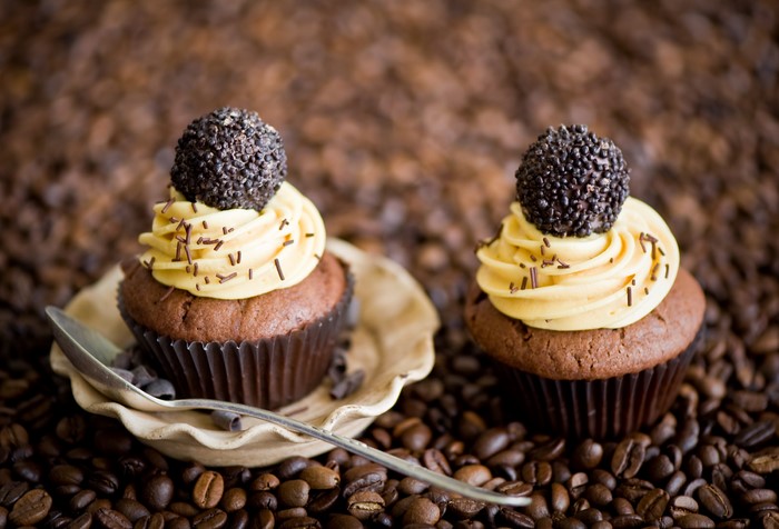 Two chocolate cupcakes with cream and chocolate balls on coffee beans