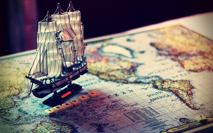 Model sailboat on a world map with Scrabble tiles spelling TRAVEL