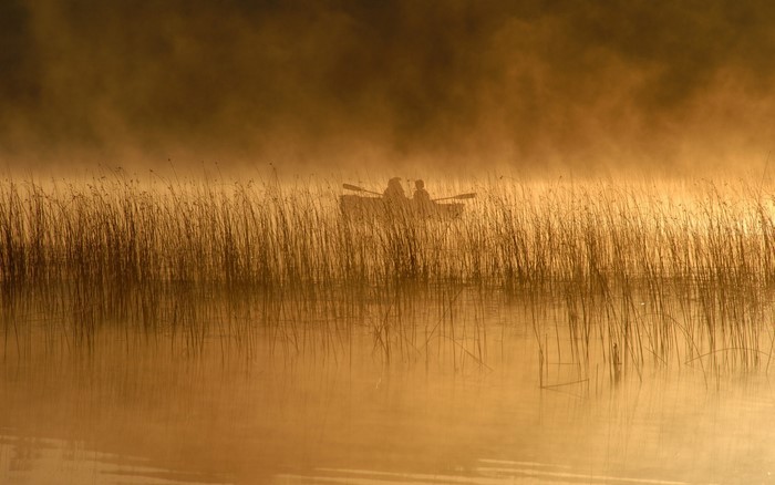 Two people in a boat on a misty lake at sunrise