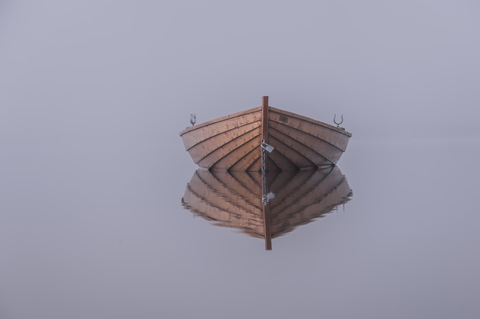 Wooden boat on foggy water with reflection