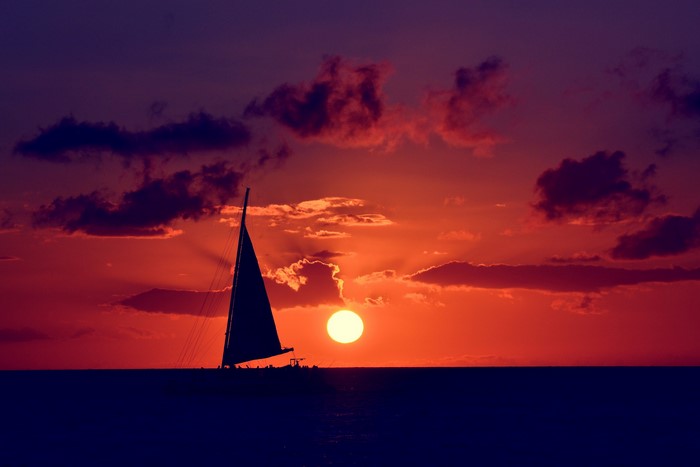 Sailboat silhouetted against a vibrant sunset over the ocean