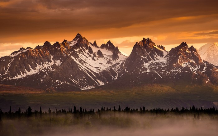 Snow-capped mountains at sunset with forest and fog