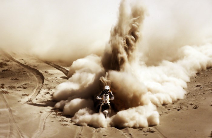 Motorcycle rider kicking up dust in a desert race