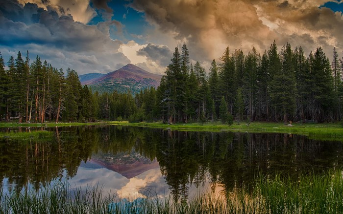 Mountain lake reflection with pine trees and dramatic clouds