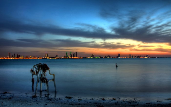 Chair in the sea at sunset with city skyline