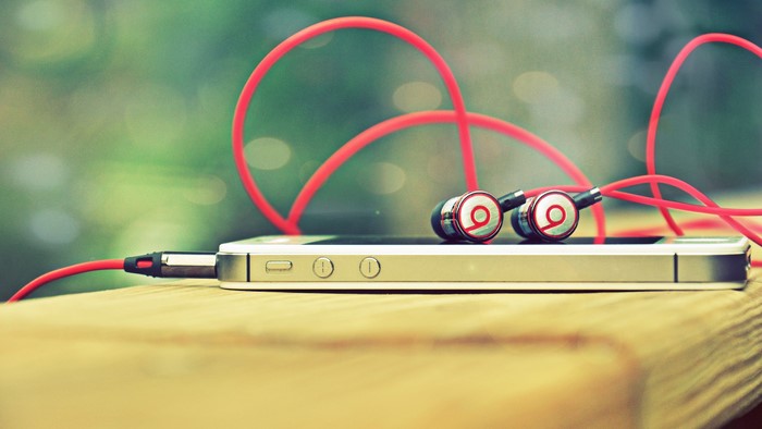 iPhone with red Beats headphones on wooden surface