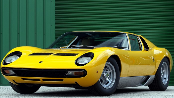 Yellow Lamborghini Miura parked in front of a green garage door