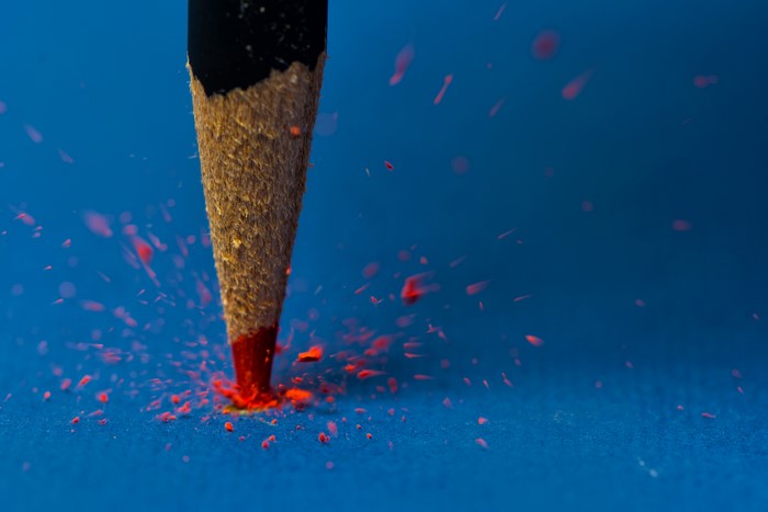 Close-up of a red pencil breaking on a blue surface