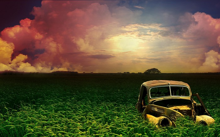 Abandoned car in a field at sunset