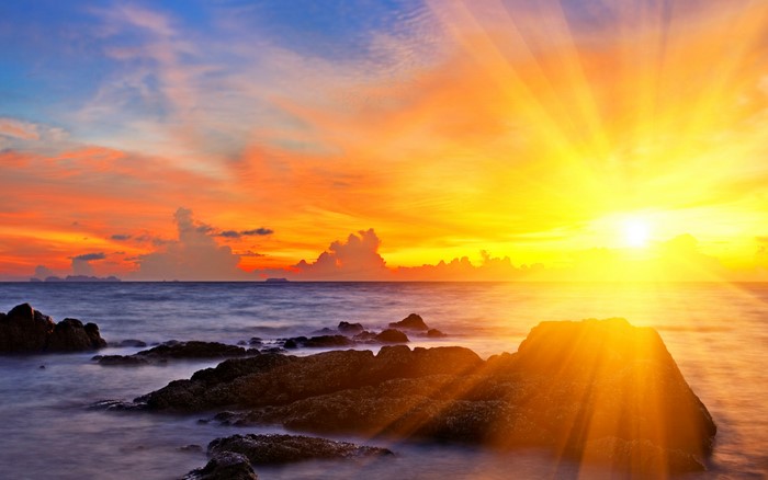 Sunset over the ocean with sunbeams and rocks