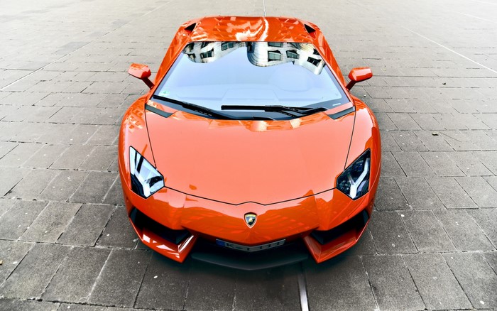 Orange Lamborghini Aventador parked on stone pavement