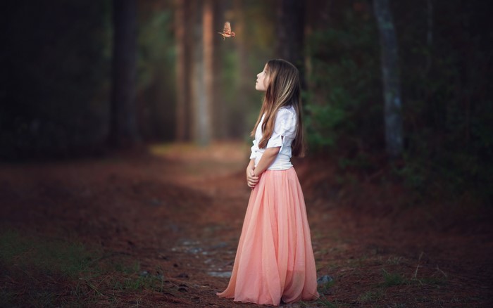 Girl in a peach skirt looking at a bird in a forest