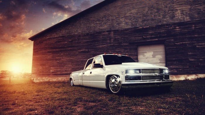 White Chevy Truck parked by a wooden barn at sunset