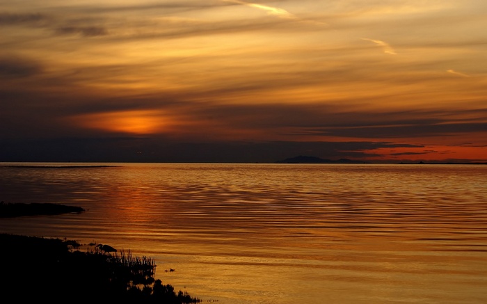 Sunset over a calm body of water with silhouetted shore