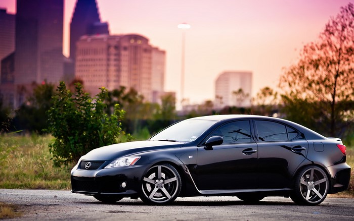 Black Lexus IS sedan with custom wheels in city at sunset